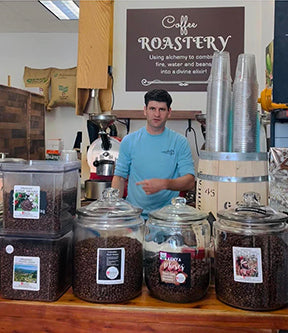 The roastery counter, staff member, and coffee bean bins at 3 Baristas